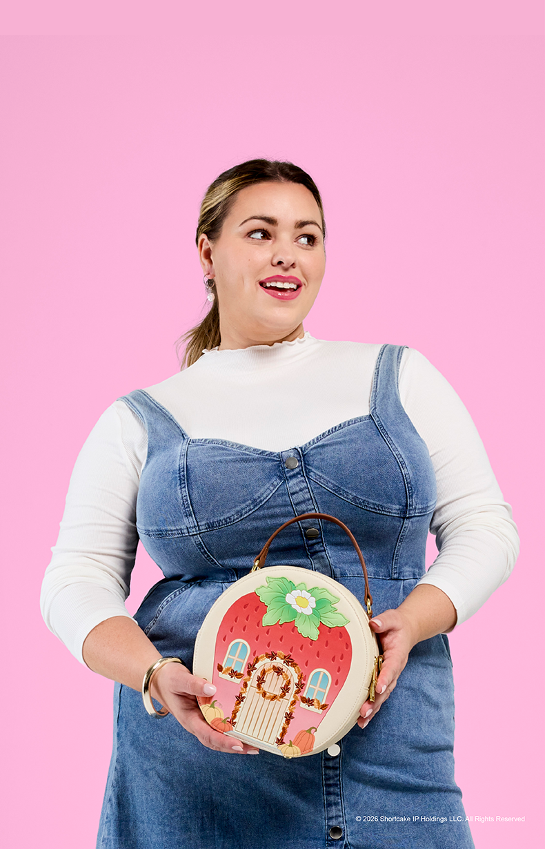 Model holding a Strawberry Shortcake Loungefly strawberry house crossbody bag.