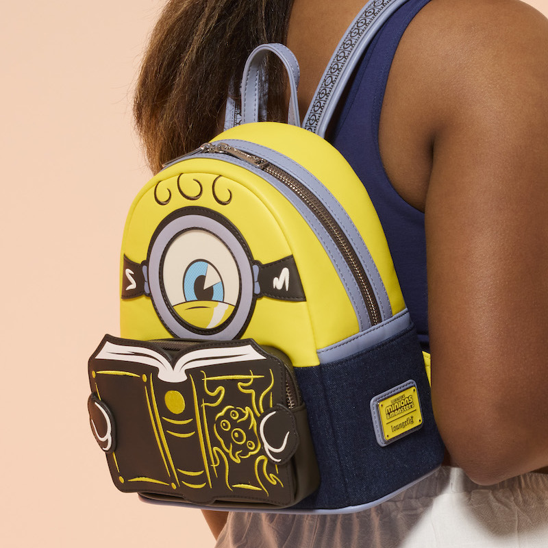 Woman facing away from camera wearing a blue top and white pants. She wears the Loungefly Minions and Monsters Mini Backpack 