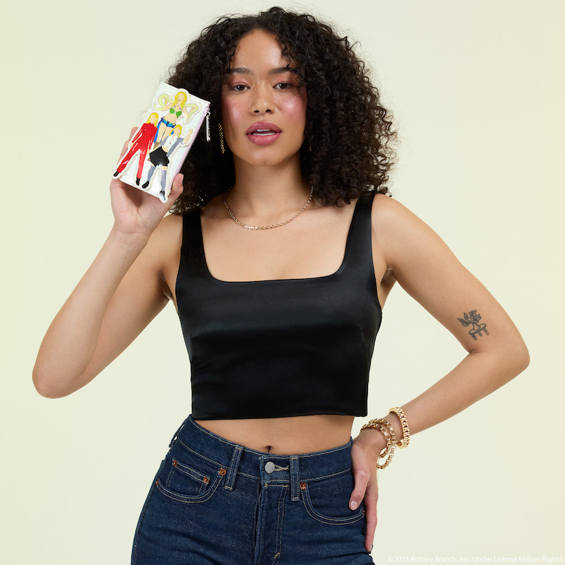 Woman posing in front of camera wearing a black crop top and dark denim jeans. She holds the Loungefly Britney Spears Classic Eras Large Card Holder up with one hand. She stands against a light green background. 