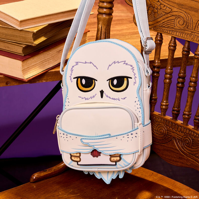 Loungefly Crossbuddies crossbody bag featuring an appliqué of Hedwig from Harry Potter. The bag hangs on a wooden chair.