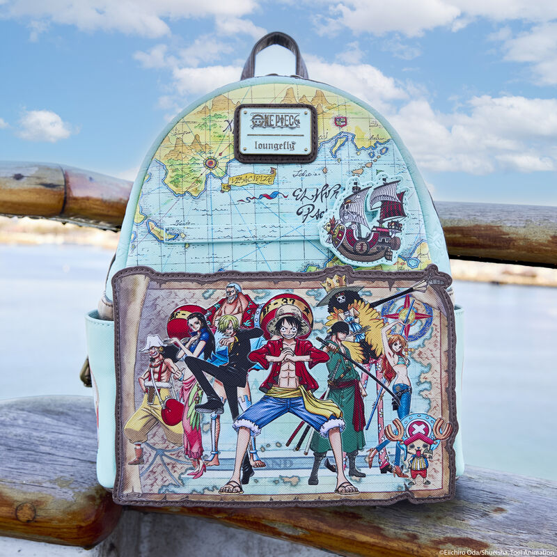 Loungefly One Piece mini backpack featuring many of the characters from One Piece, including Luffy, Chopper, Brook, and more against an appliqué parchment map. The mini backpack features a map design all over. The bag sits on a stone at the beach. 