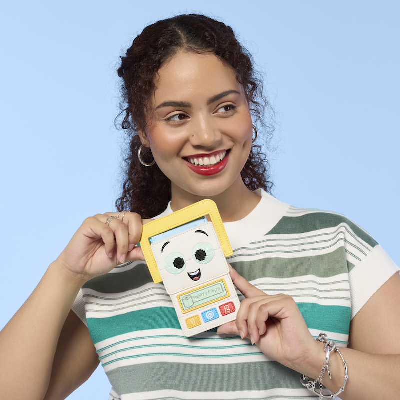 Woman smiling, looking off to the side. She wears a green-and-white striped top. She holds the Loungefly Pixar Toy Story 5 Smarty Pants Card Holder. 