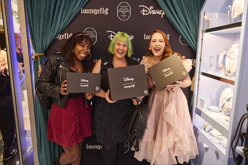Three women posing together smiling and holding black boxes featuring their raffle prizes, parts of the Loungefly Disney Swarovski collection