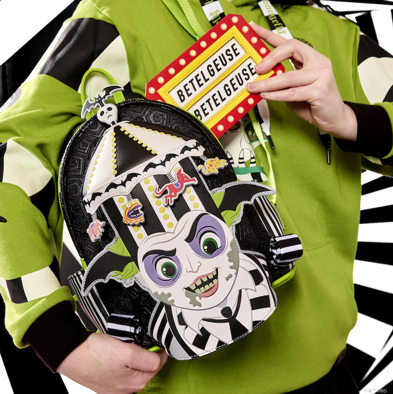 Person wearing the Loungefly Beetlejuice Unisex Hoodie and holding the Beetlejuice Carousel Hat Light Up Cosplay Mini Backpack and the Betelgeuse Marquee Card Holder. They are putting the card holder into the bag while standing against a black and white background. 