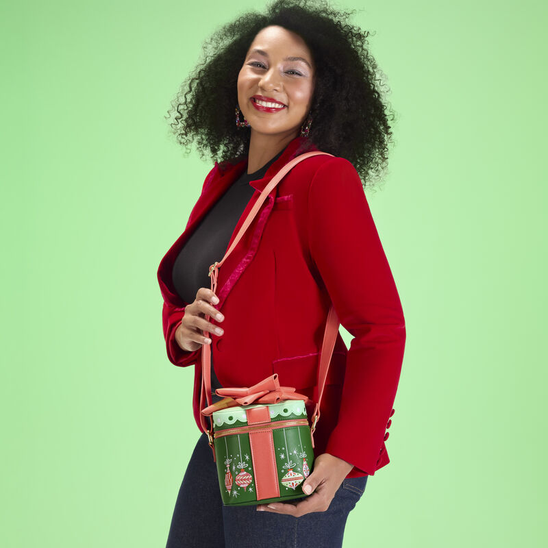 Woman wearing jeans, black top, and red blazer, wearing the Loungefly Holiday Gift Figural Crossbody Bag. She stands against a green background.  