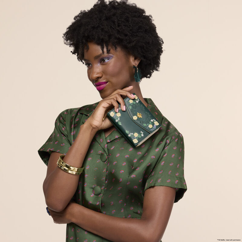 Woman wearing a green silk dress, looking off to the side, holding the Loungefly Bridgerton Floral Zip Around Wallet in one hand. 