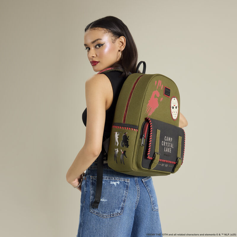 Woman facing sideways to camera, looking over her shoulder at camera wearing a black tank and blue jeans. She wears the Loungelfy Friday the 13th Camp Crystal Lake Canvas Full-Size Backpack on her back. 