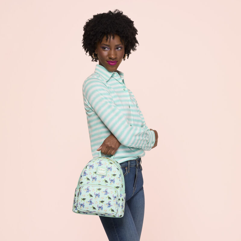 Woman wearing a light blue and white striped shirt with jeans. She holds the Loungefly Disney Lilo and Stitch Animal Friends All Over Print Mini Backpack. 