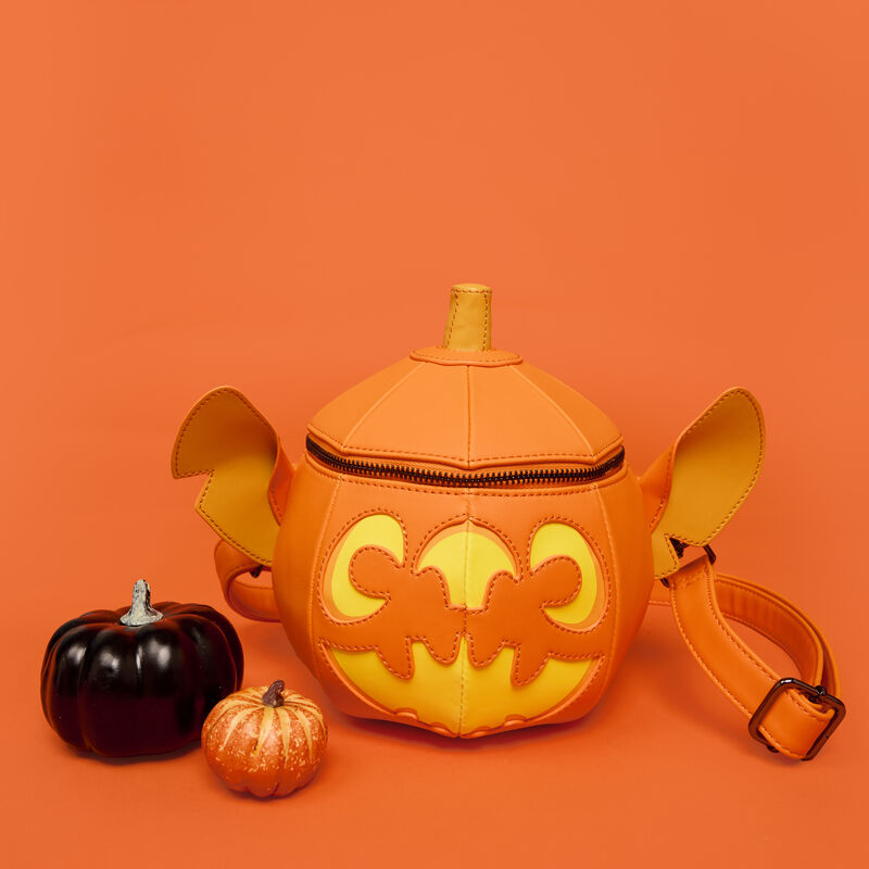 Figural Loungefly crossbody bag that looks like a Stitch-shaped jack-o'-lantern. The bag stands against an orange background and sits beside two mini pumpkins. 