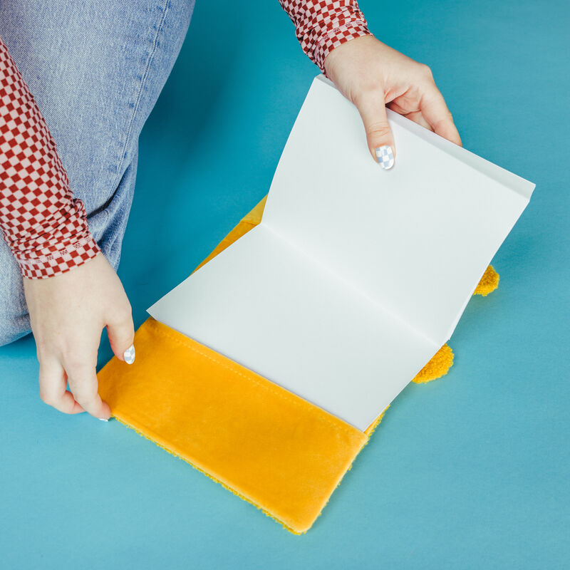 Someone inserting a journal refill into a plush Winnie the Pooh journal cover against a blue background