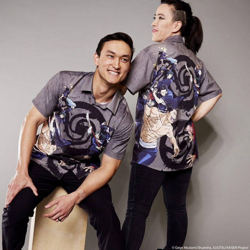 Man and woman modeling the Loungefly JUJUTSU KAISEN Sorcerer Battle Camp Shirt. The man sits on the left, looking off camera. The woman stands to the right, facing away from camera with her arm resting on the man's shoulder to show off the back of the shirt. 