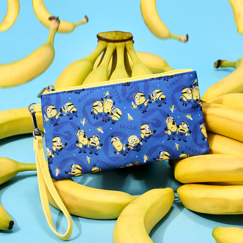 Nylon Loungefly Minions wristlet featuring various Minions and bananas against a blue background. The wristlet sits on a pile of bananas with a blue background. 