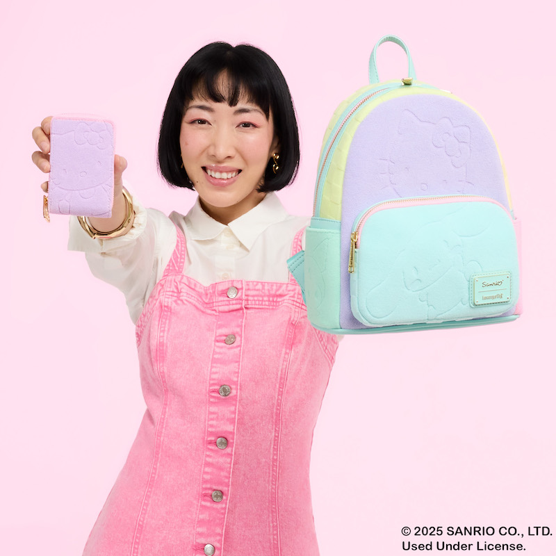 Woman smiling at camera holding up the Loungefly SDCC Limited Edition Hello Kitty & Friends Color Block Terry Cloth Mini Backpack and Accordion Wallet out toward camera. She stands against a pink background.