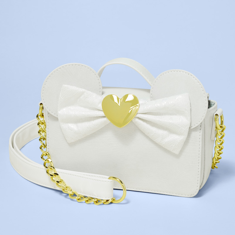 Loungefly Minnie Mouse Iridescent Lace Wedding Crossbody Bag, featuring 3D applique Minnie Mouse ears and a lace bow with a golden heart in the center. The bag sits against a light blue background. 