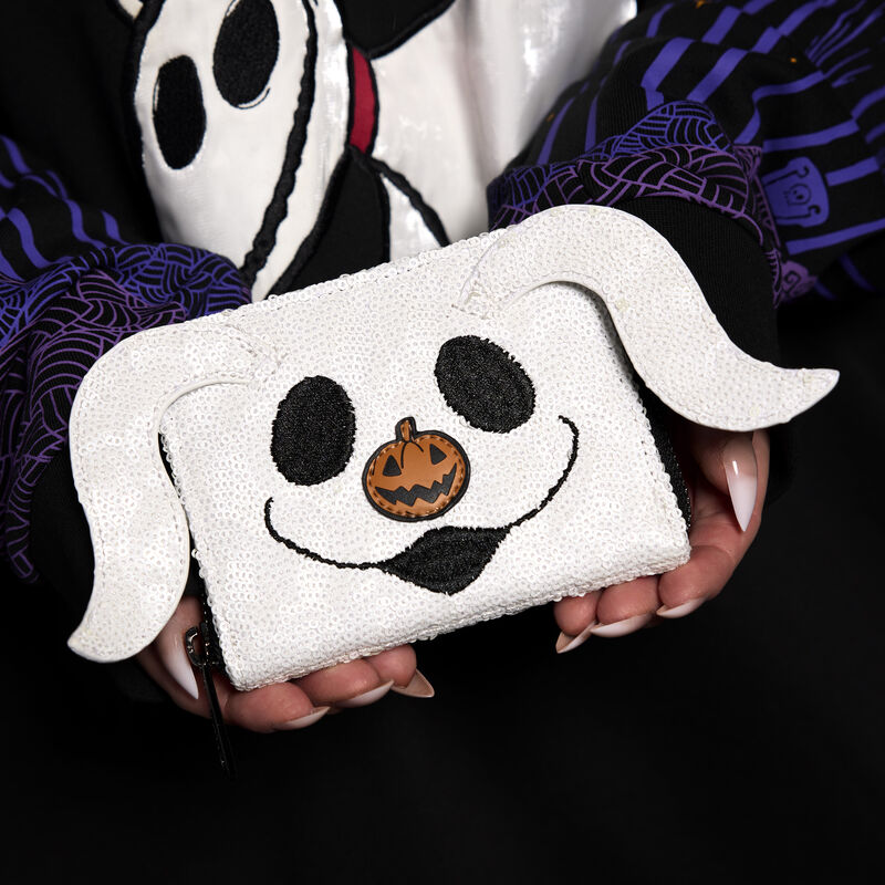 Close-up shot of a woman holding the sequin, glow-in-the-dark Loungefly wallet featuring Zero from The Nightmare Before Christmas.