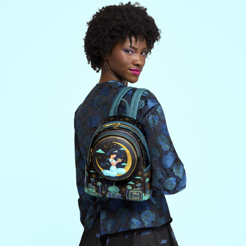 Woman facing away from camera wearing a blue jacket. She looks over her shoulder at the camera and wears the Exclusive Loungefly Disney Princess Jasmine Moonlit Palace Mini Backpack. 
