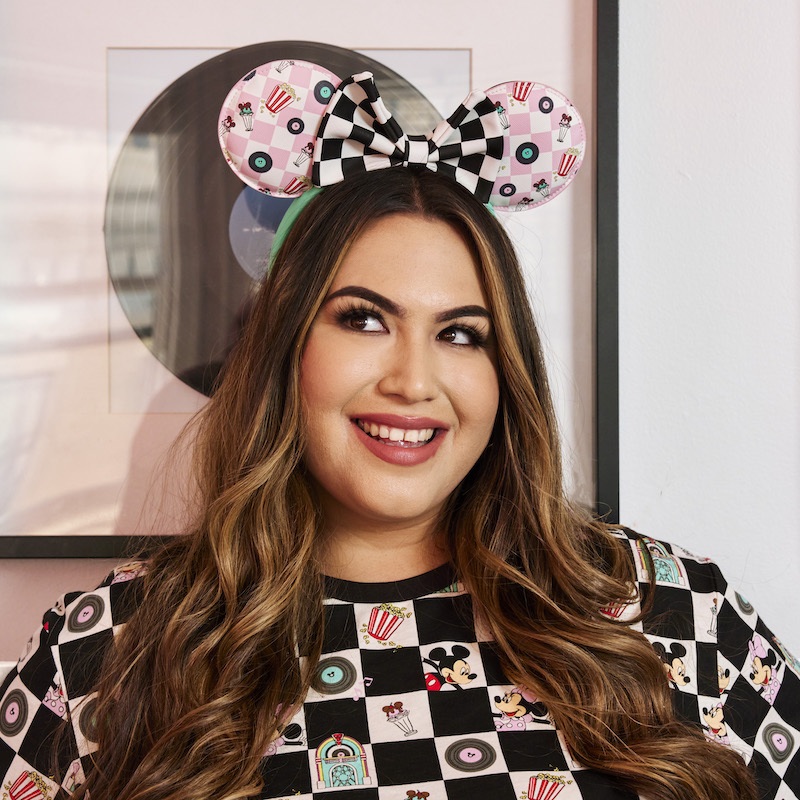 Image of woman wearing the Mickey and Minnie Date Night Diner Jukebox Record Ear Headband with the pink checkered print side facing forward 