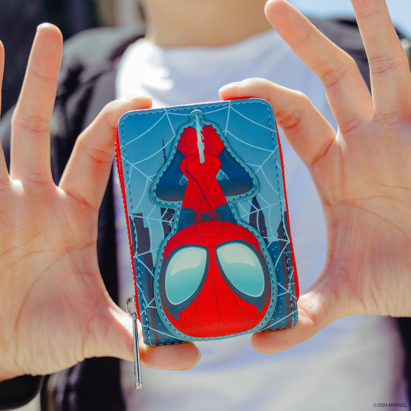 Person standing outside holding the SDCC Spider-Man Glow Accordion Zip Around Wallet toward the camera, featuring Spider-Man hanging upside down on the front. 