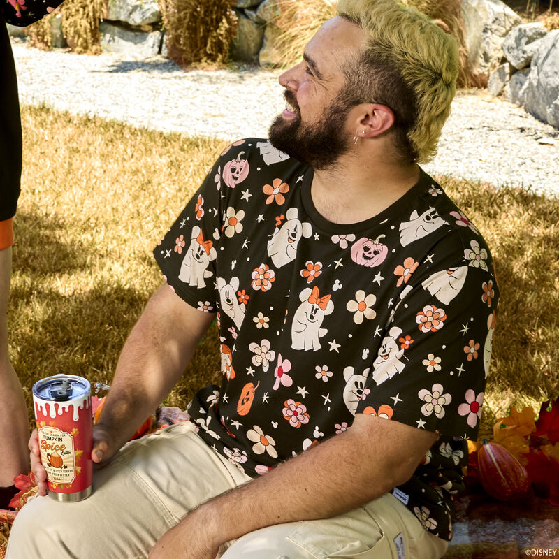 Man sitting outside, looking up and smiling at a friend, wearing the Loungefly Mickey & Minnie Floral Ghost Tee, featuring an all-over pattern of Mickey and Minnie as ghosts among pumpkins and stars.