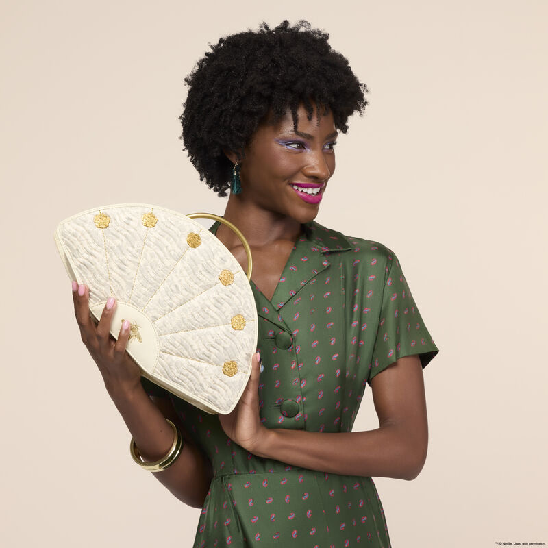 Woman smiling and looking off to the side, wearing a green silk dress and holding the Loungefly Bridgerton Figural Fan Handbag. 