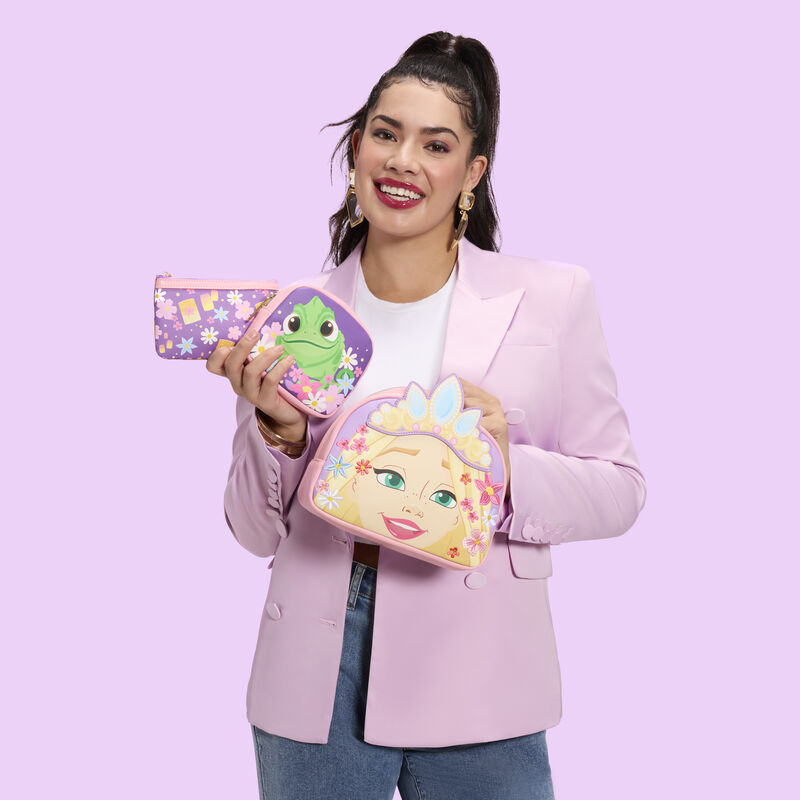 Woman wearing a pink blazer, white top, and jeans, holding the Loungefly Rapunzel Cosmetic Bag Set. She stands against a pink background. 
