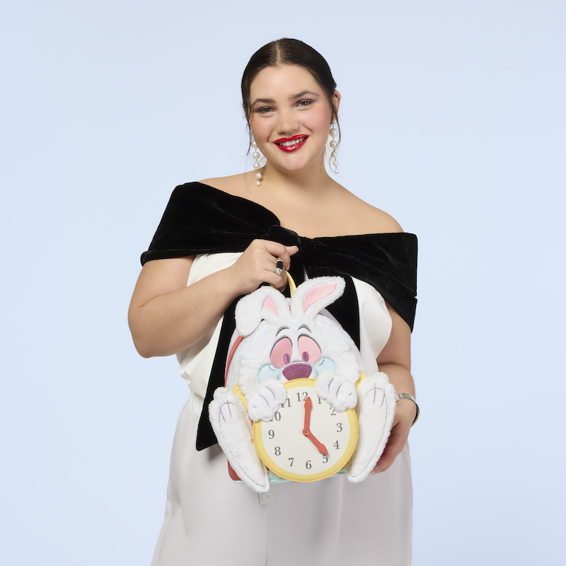 Woman wearing white pants and a black-and-white off-the-shoulder top, holding the Loungefly Alice in Wonderland White Rabbit mini backpack. 