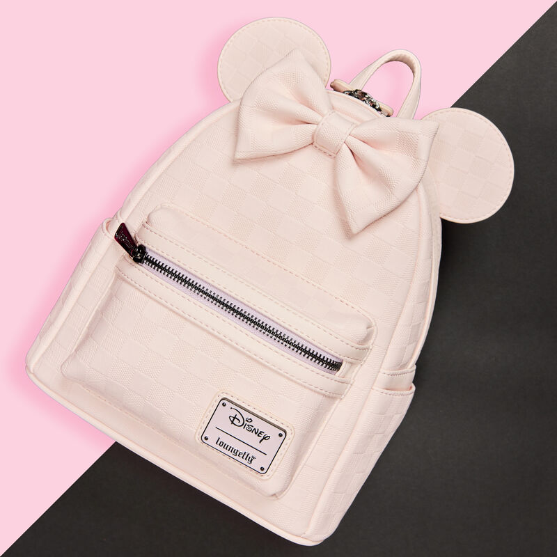 Light pink Loungefly Minnie Mouse mini backpack featuring a textured checkerboard pattern. The bag sits against a pink and black background.