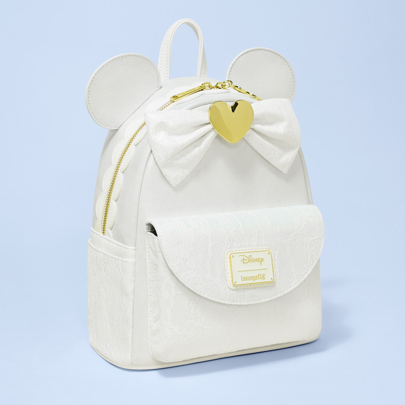 White mini backpack featuring lace on the front and side pockets, 3D applique Minnie Mouse ears, and a lace bow with a golden heart in the center. The bag sits against a light blue background. 