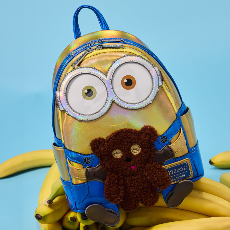 Iridescent Minions Bob mini backpack sitting on a pile of bananas, featuring Bob from Minions holding his brown teddy bears