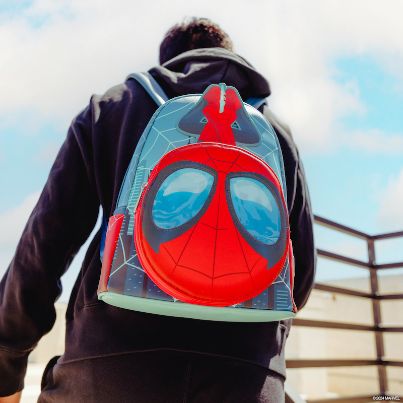 Man outside on a balcony wearing a hoodie and the SDCC Spider-Man Lenticular Glow Mini Backpack, featuring Spider-Man hanging upside down