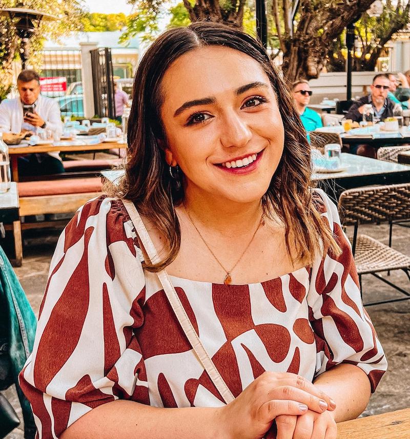 woman with shoulder-length brown hair sitting at a table and smiling at the camera, wearing a red and white patterned dress