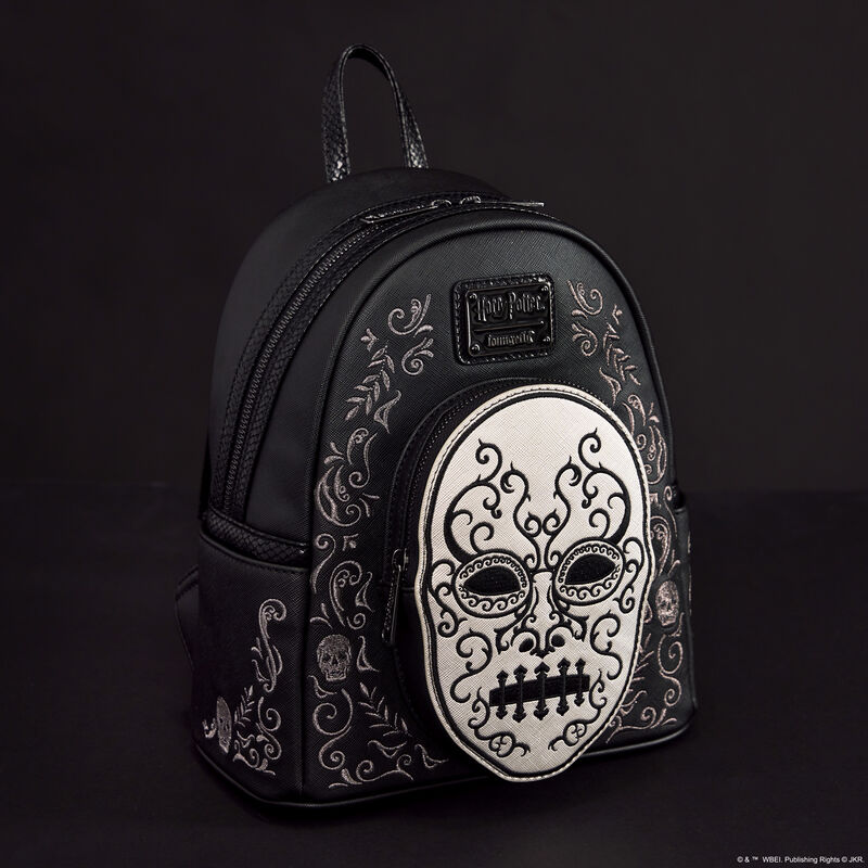 Black Loungefly mini backpack featuring a silver Death Eater mask as the front pocket with embroidered symbols around it. The bag sits against a dark background.