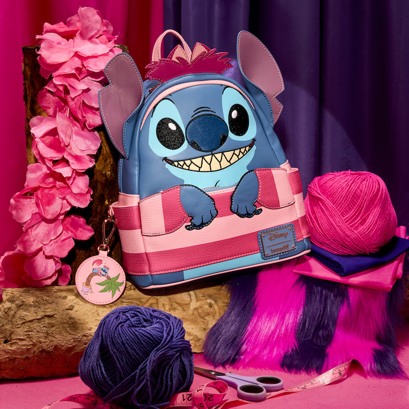 Loungefly mini backpack featuring Stitch dressed as the Cheshire Cat from Alice In Wonderland. The bag sits among purple and pink sewing materials. 