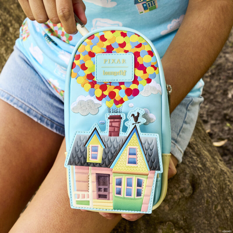 Person sitting on a rock outside holding the Loungefly Pixar Up 15th Anniversary Balloon House Stationery Mini Backpack Pencil Case, featuring Carl and Ellie's house attached to a bunch of balloons. 