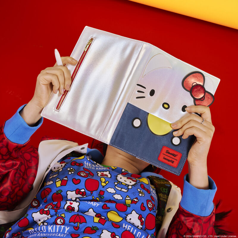 Woman laying on her back against a red background, holding the Hello Kitty refillable journal open above her head with a pen in her hand