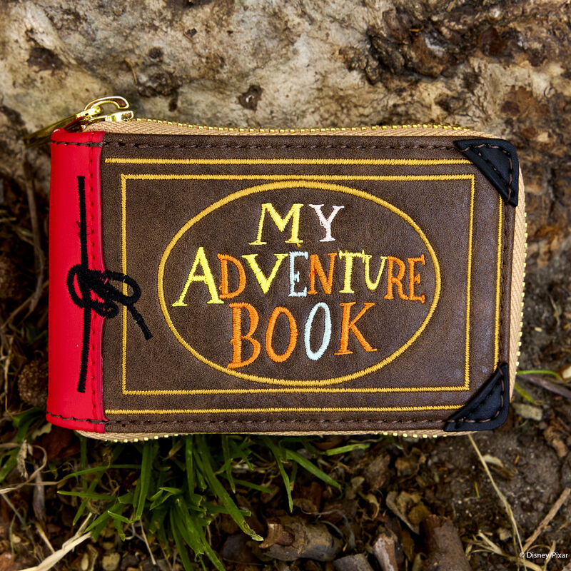 Loungefly Pixar Up 15th Anniversary Adventure Book Accordion Zip Around Wallet sitting against a rock along the grass. 