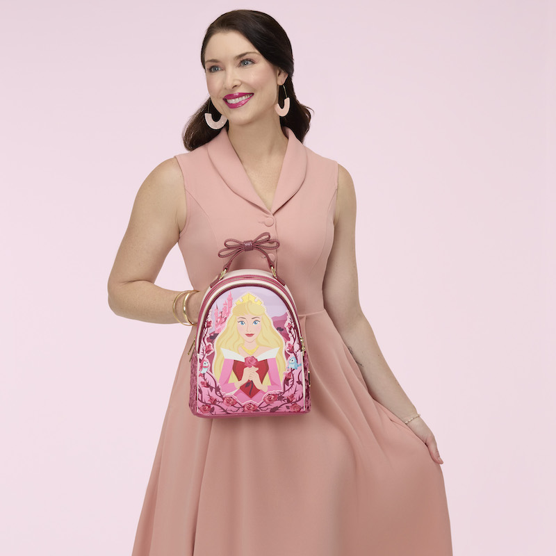 Woman in a pink dress holding the Loungefly Disney Sleeping Beauty Exclusive Mini Backpack. 