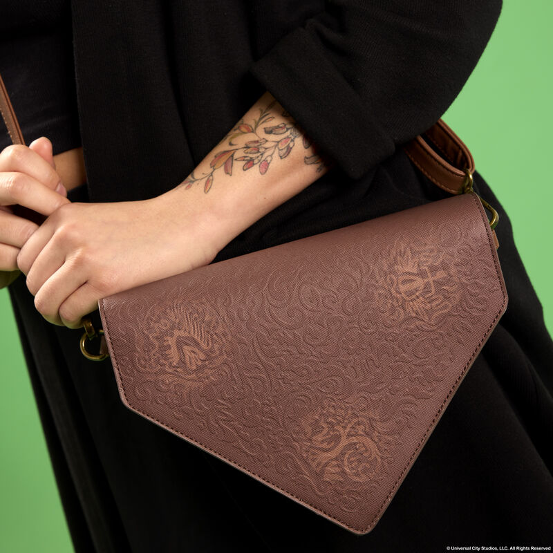 Woman standing against a green background wearing all black and wearing the Loungefly Wicked Elphaba's Grimmerie Spell Book Crossbody Bag.