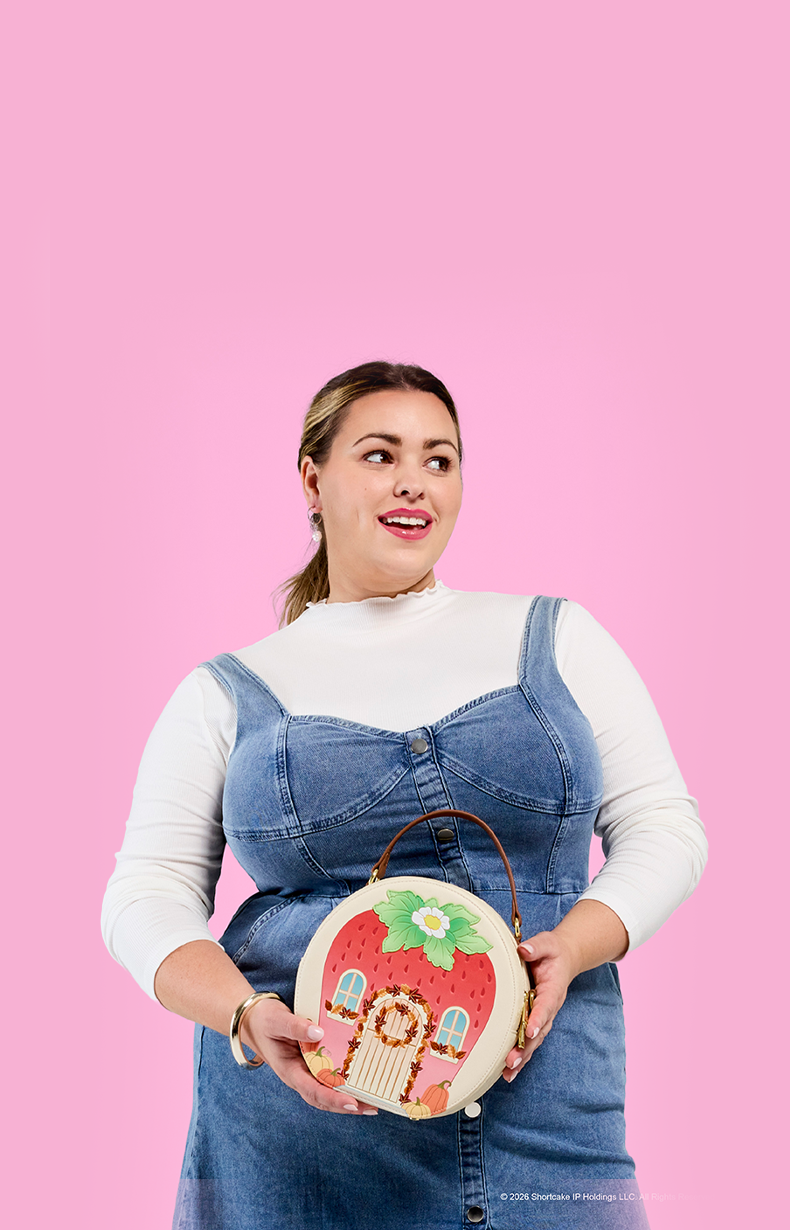 Pink background with model in denim overalls showcasing Loungefly Strawberry Shortcake bag