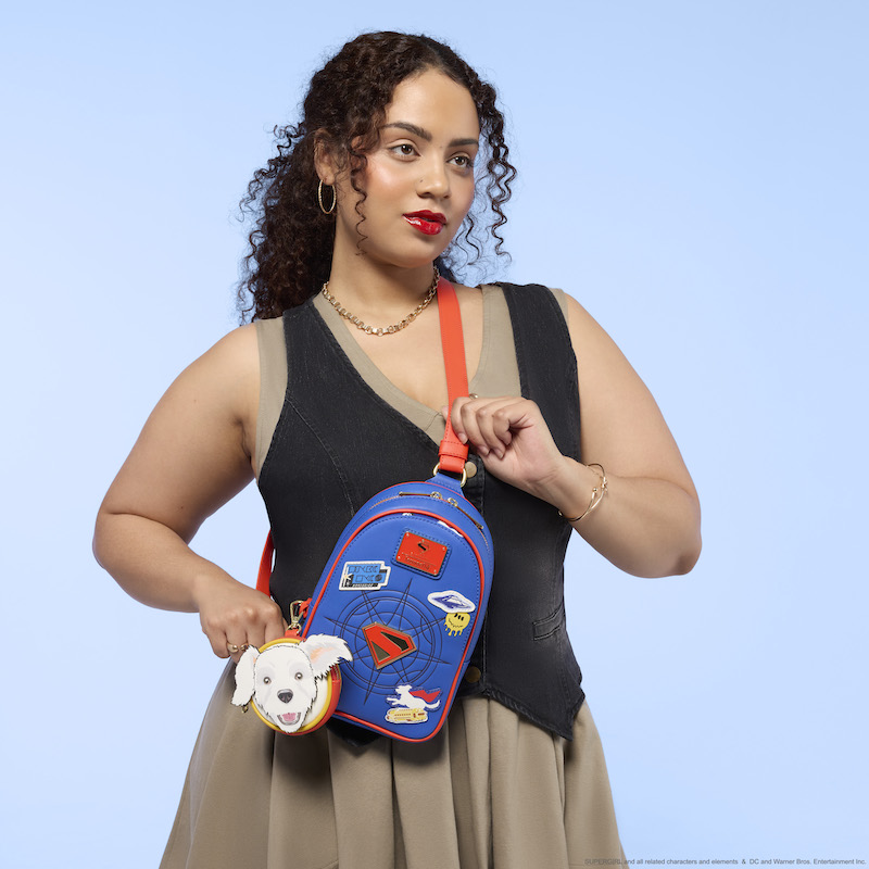 Woman wearing a khaki-colored dress with black vest, wearing the Loungefly DC Supergirl Krypto Sling Crossbody bag. 