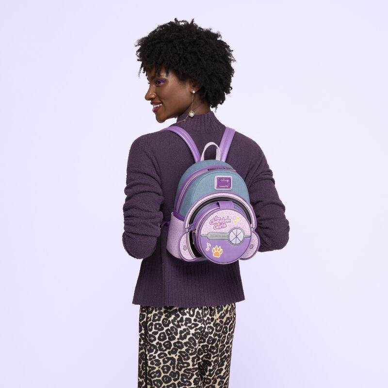 Woman facing away from camera, wearing a purple top and cheetah print bottoms. She wears the Loungefly Cheetah Girls mini backpack on her back. 