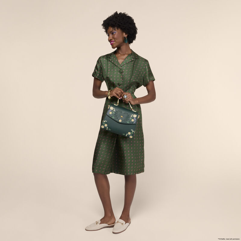 Woman wearing a green silk dress and holding the Loungefly Bridgerton Floral Crossbody Bag in both hands. 