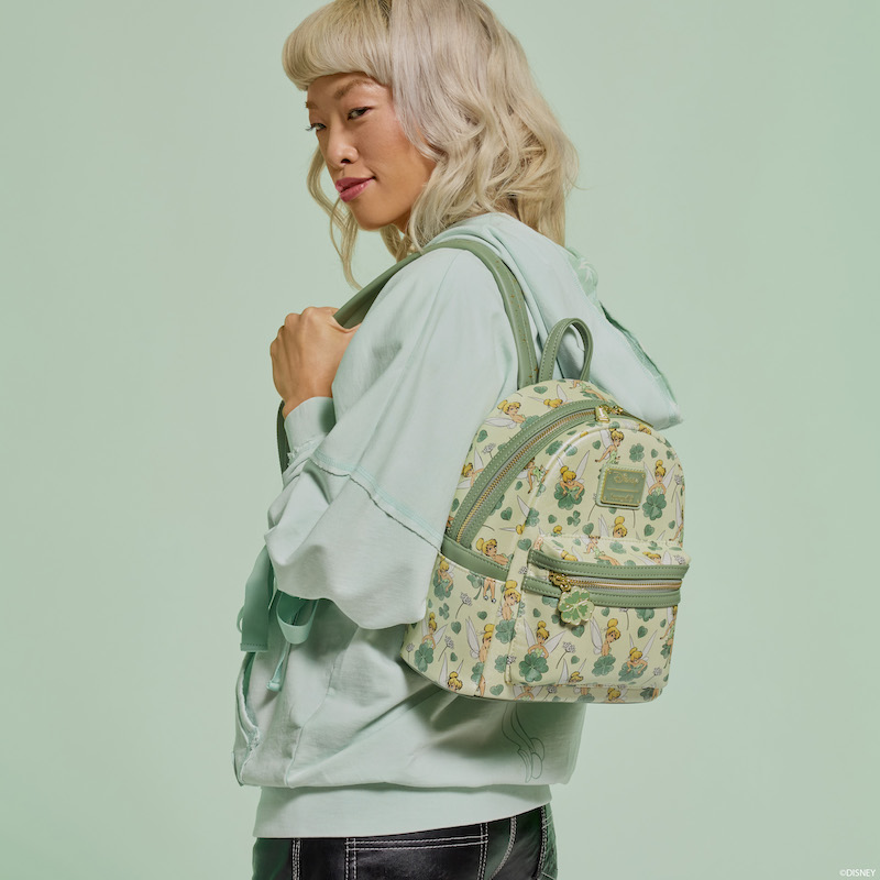 Woman facing to the left, wearing the Loungefly Peter Pan Tinker Bell Clover mini backpack. She stands against a light green background. 