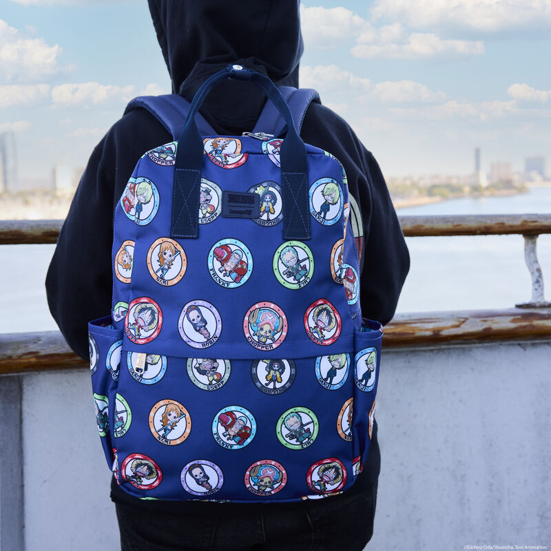 Person standing outside wearing a hoodie and facing away from camera wearing the Loungefly One Piece 25th Anniversary Backpack, featuring each of the different characters in circle designs all over the bag. 