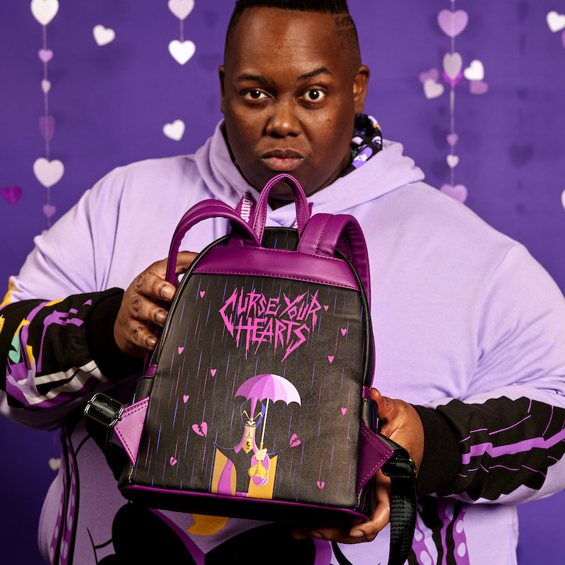 Image of man holding the Loungefly Disney Villains Curse Your Hearts Mini Backpack and showing the back of the bag toward camera to reveal the artwork of Jafar with "Curse Your Hearts" written above him