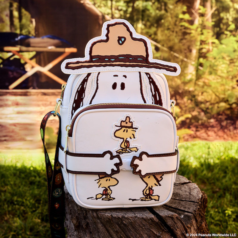 Snoopy Beagle Scouts Crossbuddies Bag sitting on a tree stump at a camp ground, featuring Snoopy in appliqué detail with a Beagle Scout hat and holding the reversible coin bag with the image of Beagle Scouts facing the front.  