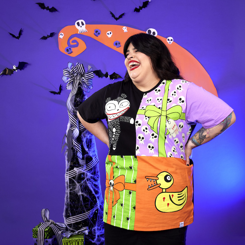 Woman wearing the Nightmare Before Christmas Toys Unisex Tee against a purple and orange background with bats and a spooky tree.