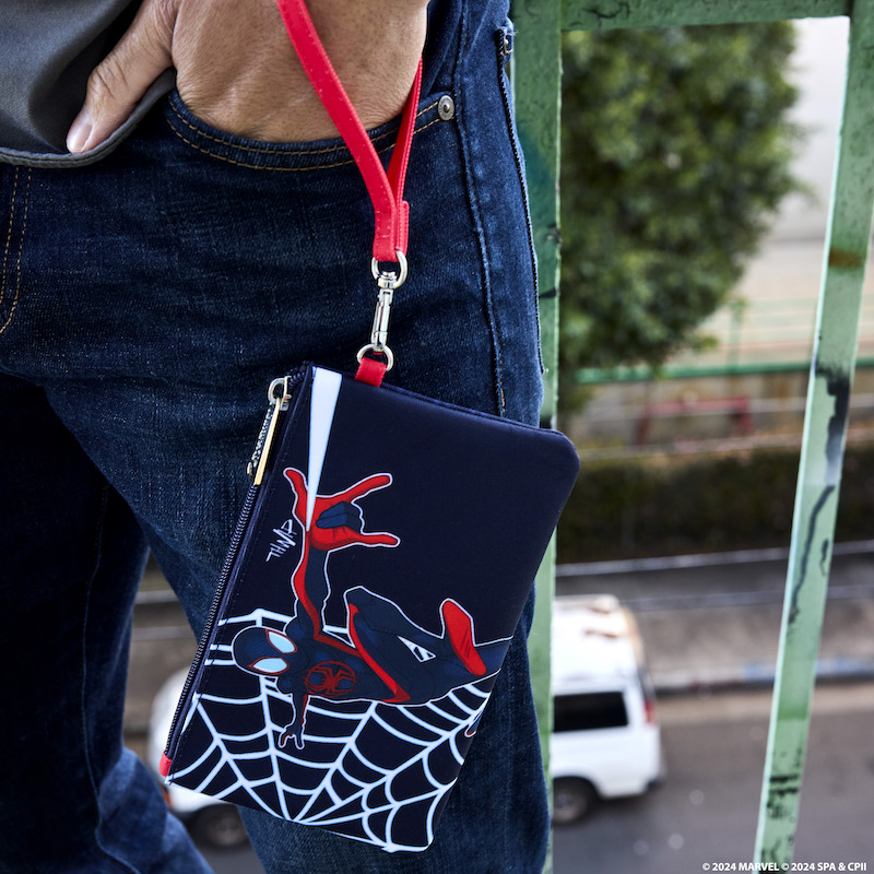 Man standing outside with the Miles Morales nylon pouch wristlet around his wrist with a hand in his jeans pocket. The wristlet features Miles as Spider-Man with a web behind him. 