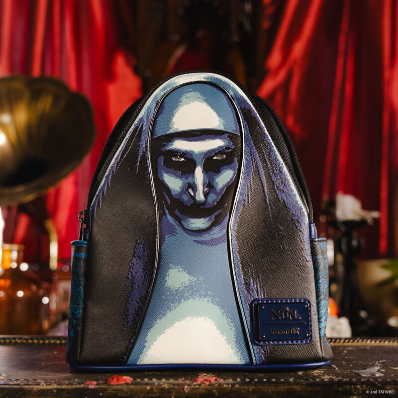 Loungefly mini backpack featuring The Nun on the front in appliqué detail. It sits in front of a red curtained background. 