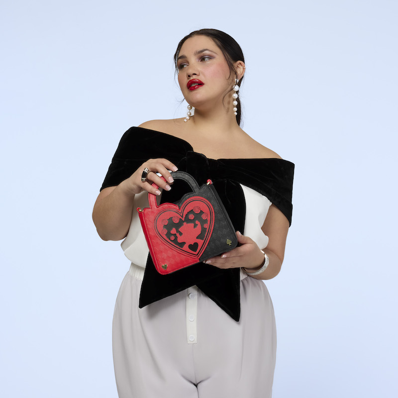 Woman wearing white pants and a black-and-white off-the-shoulder top. She holds the Loungefly Alice in Wonderland Queen of Hearts Crossbody bag in both hands. 